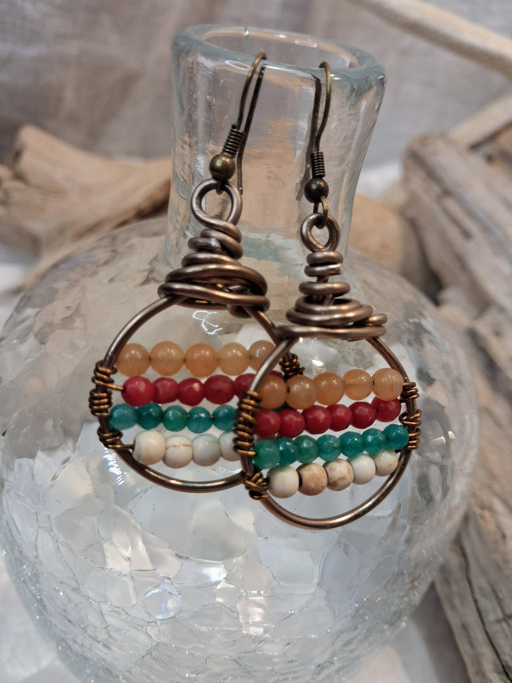 Amber, red, teal and white beaded boho hoop earrings with wire-wrapped metal frames, handmade by Melly