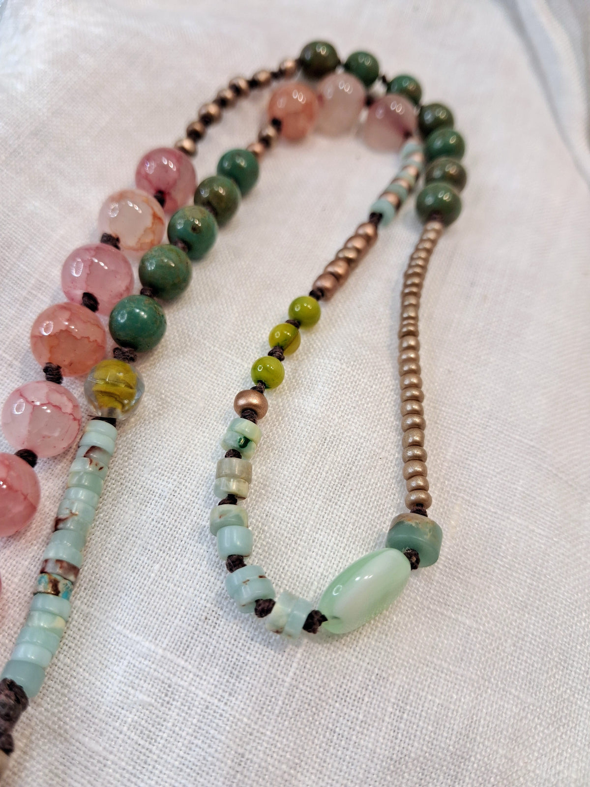 Pink and green stone beaded necklace featuring metallic spacers on brown cord, handmade by Melly