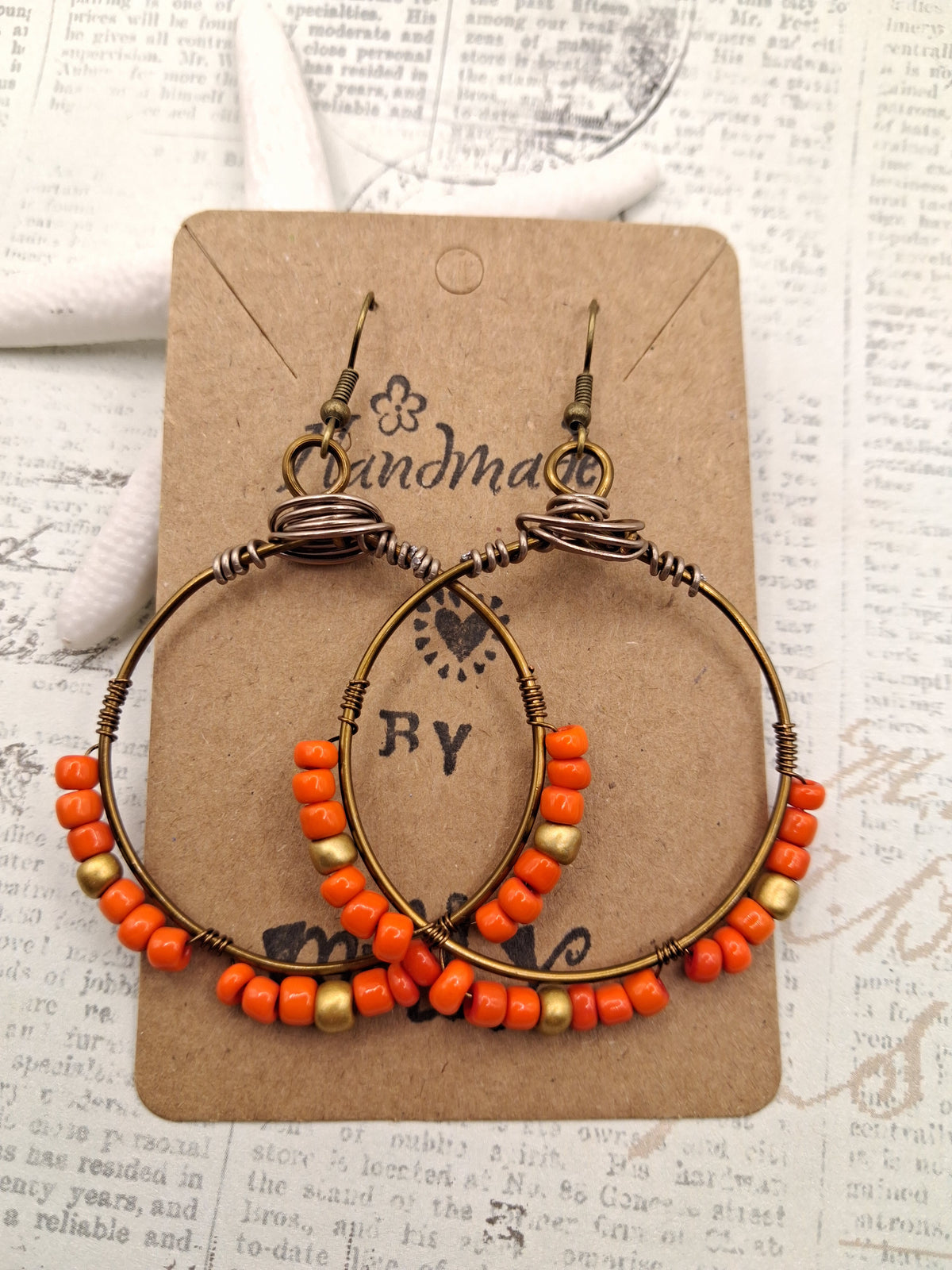 Orange and gold beaded hoop earrings featuring wire-wrapped metal and seed beads, handmade by Melly