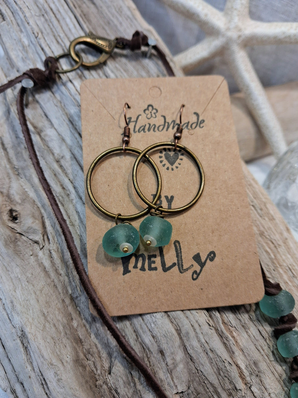 Teal sea glass and brass hoop earrings displayed on a brown card, handmade by Melly