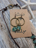 Teal sea glass and brass hoop earrings displayed on a brown card, handmade by Melly