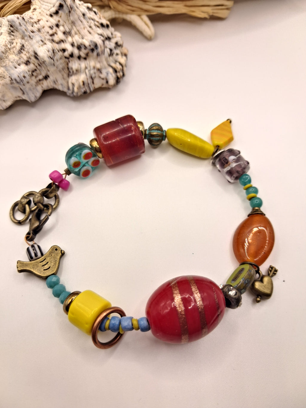 Teal and red beaded love charm bracelet featuring mixed glass beads and a bird charm, handmade by Melly