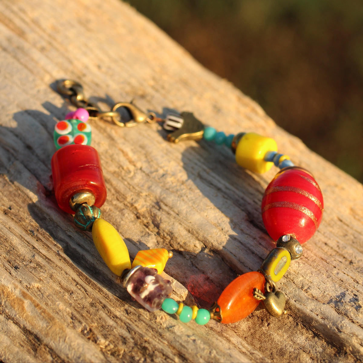 A colorful beaded bracelet with red, yellow, orange, and turquoise beads, resting on a weathered wooden surface with a blurred outdoor background.
