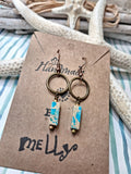 A pair of handmade dangle earrings displayed on a brown kraft card. The earrings feature bronze-toned metal rings, copper wire wrapped hooks, and rectangular turquoise and cream marbled impression jasper beads.