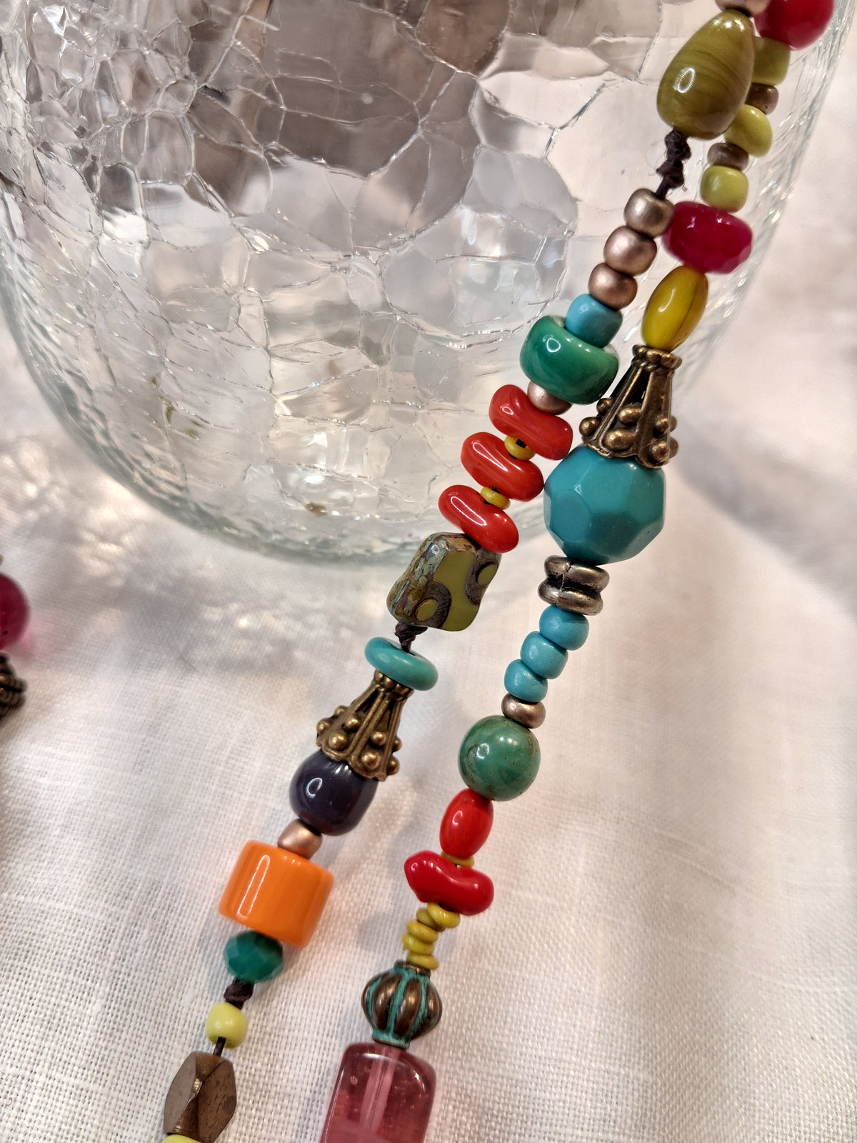 Close-up of a multi-color beaded necklace featuring glass and metal beads, handmade by Melly