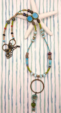 Turquoise, teal, and olive beaded sea shore necklace featuring metal and glass components handmade by Melly